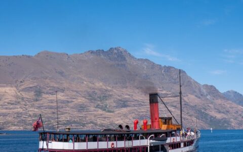 A steamboat sails across the water near a mountain.